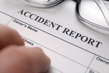 Close-up of hands and glasses on an 'ACCIDENT REPORT' form, signifying filing.